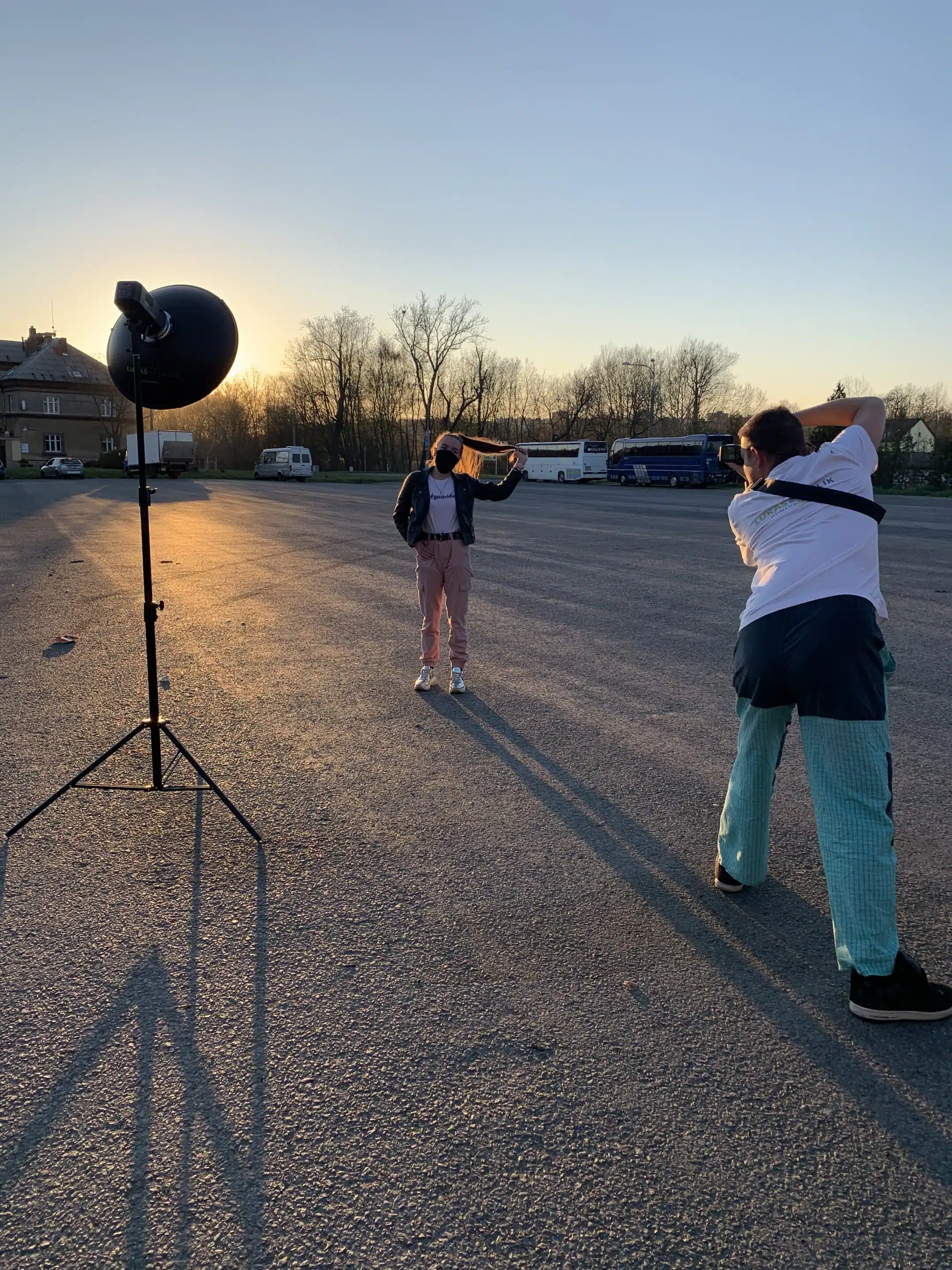 lukasstehlik-00005 Fotograf fotí osobu pózující na prázdném parkovišti při západu slunce, poblíž je rozmístěno osvětlovací zařízení.